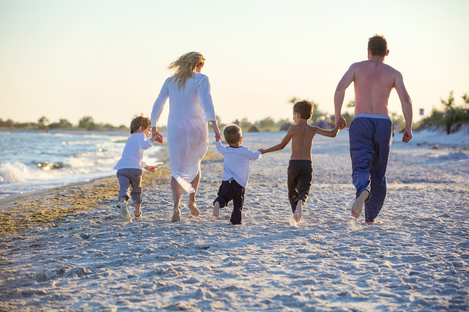 Happy young family holding hands and running on beach before sunset